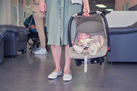 A mother with a newborn baby in a carrier is waiting for a doctor appointment in the lobby of the clinic. The parent keeps the child in the infant car seat when visiting the hospitalの写真素材