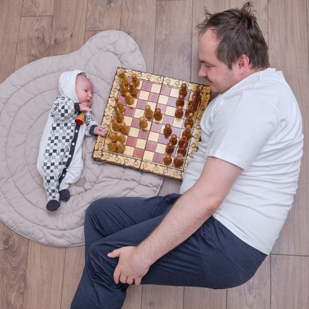 Man father and newborn baby boy near the chessboard with placed chess pieces