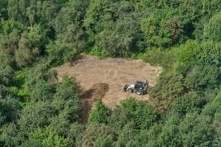 The excavator prepares the soil on the field in the forest among the trees for landscaping and agriculture, top view - Moscow, Russia, August 24, 2021のeditorial素材
