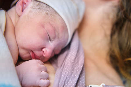 Head of a newborn baby close-up. Laying the child out on the mother chest immediately after childbirth. A woman who gave birth to a newborn baby boyの写真素材