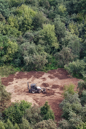 The excavator prepares the soil on the field in the forest among the trees for landscaping and...