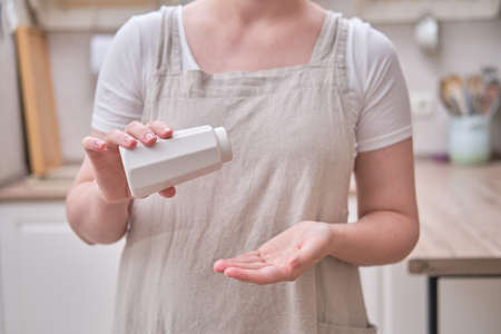 A white salt shaker in the hands of a woman in the kitchen. Female hands hold ceramic pepper shakerの写真素材