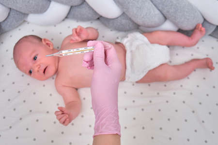 Doctor checks the temperature of the newborn baby with a thermometer. A nurse in uniform measures the child fever with a thermometerの写真素材