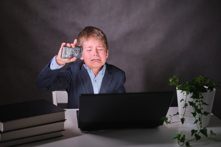 A boy with a broken mobile phone, copy space on a dark studio background