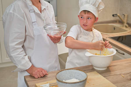 Mother and son cooking apple pie in the home kitchen. A woman and a boy in chef hats and aprons cook with pastriesの写真素材