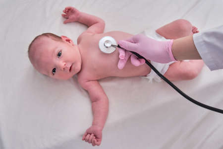 Woman doctor listens with a stethoscope to a newborn baby. Nurse checks the child health with a stethoscopeの写真素材
