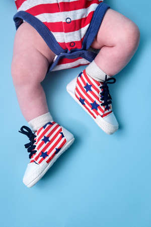 A newborn baby shoes in the colors of the American flag of the United States, blue studio background. A child in the boots of the red and white USA flagの写真素材