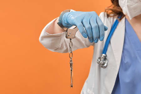 Doctor hands in handcuffs on red background, closeup. Woman hands in medical gloves handcuffed, coronavirus quarantine concept.の写真素材