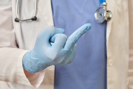 A hand in a pink medical glove shows the fuck you gesture. A doctor in a blue uniform makes an...