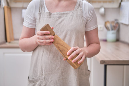 A spice mill in the hands of a woman in the kitchen. Female hands holding a wooden pepper shaker