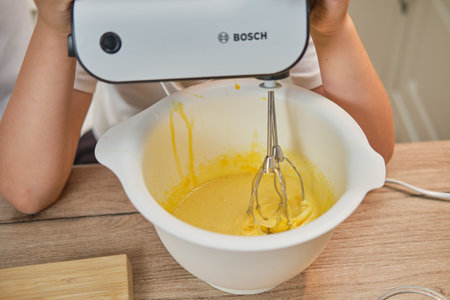 Boy in white chef clothes beats eggs with a Bosch mixer to make a pie in his home kitchen - Moscow, Russia, September 2, 2021のeditorial素材