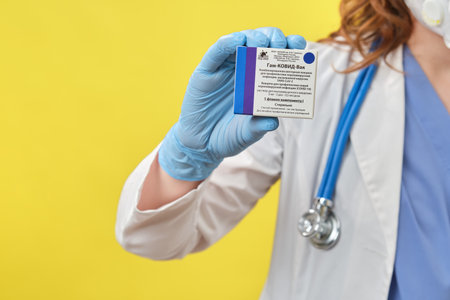A female doctor holds in her hand a pack of ampoules for vaccination Sputnik V, yellow studio background - Moscow, Russia, September 16, 2021のeditorial素材