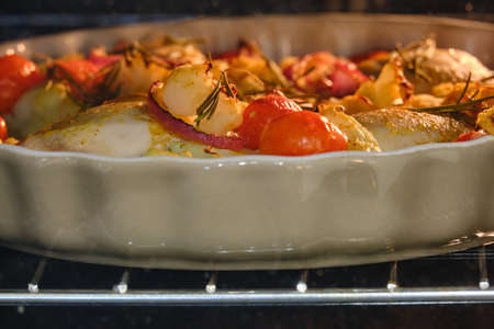 Chicken with vegetables, herbs and tomatoes is baked in the oven in a home kitchenの写真素材