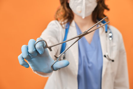 The doctor holds a surgical clamp in his hand. Nurse with a medical clip with scissors in her hand, studio backgroundの写真素材