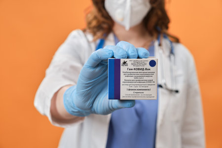 Woman doctor holds in her hand a pack of ampoules for vaccination Sputnik V, red studio background - Moscow, Russia, September 16, 2021のeditorial素材