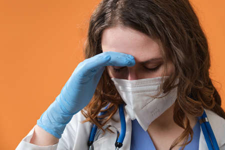 A young female doctor is tired and holding her head, copy space for the text. Portrait of a nurse on a orange background, close-up.の写真素材