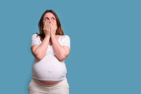 Emotion of shock in pregnant woman, studio shot on blue backgroundの写真素材