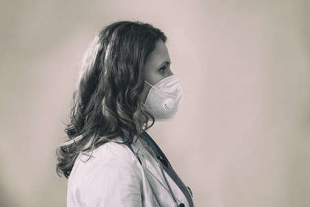 Woman doctor on a gray background, black and white. Concept of the fight against coronavirus. Face nurse in a blue uniform, portrait in profile.の写真素材