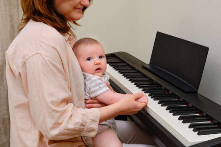 Mother with infant baby at the piano teaches son to play a musical instrumentの写真素材