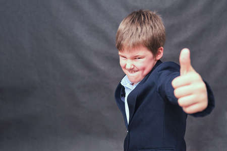 A boy in a school uniform shows a thumbs up sign on a dark backgroundの写真素材