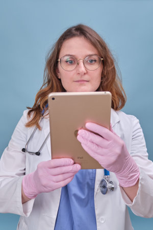 Woman doctor with a digital tablet Apple iPad in a white uniform on a blue studio background - Moscow, Russia, August 12, 2021のeditorial素材