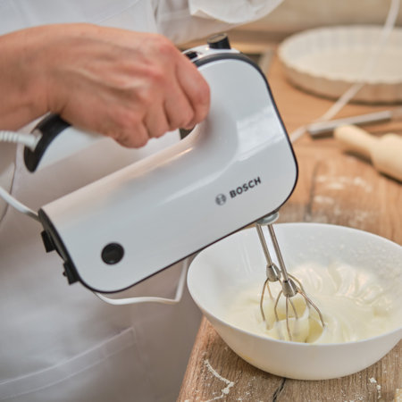 An adult woman in white chef clothes beats eggs with a Bosch mixer to make a pie in the home kitchen - Moscow, Russia, September 2, 2021のeditorial素材