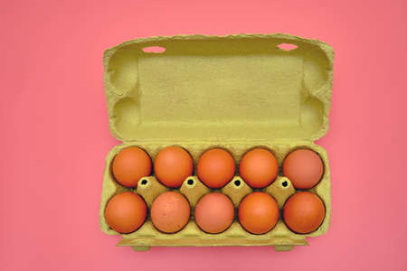 A full package of brown eggs in a cardboard box on a pink backgroundの写真素材