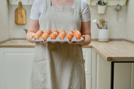 A woman holds a package with a lot of eggs standing on a home kitchen, close-up