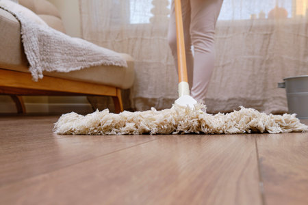 An adult woman mops a wooden laminate floor while cleaning her home living room.の写真素材