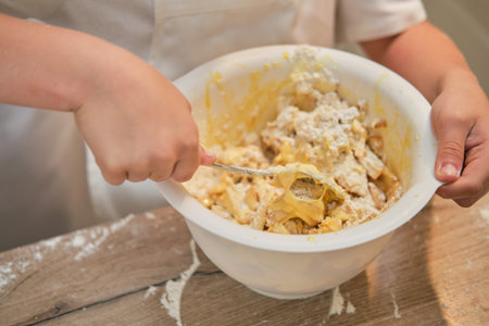 A boy in chef clothes pours flour into the dough for cooking apple pie