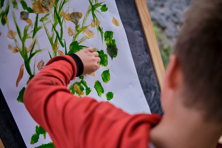 The child is learning to paint with paints on canvas, easel with paper. Boy artist paints nature