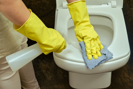 A woman cleans up the bathroom by wiping the toilet bowl with a rag. Disinfection with yellow rubber...