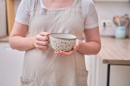 A large cup is in the hands of a woman in the kitchen. Female hands holding a cup for coffee or teaの写真素材