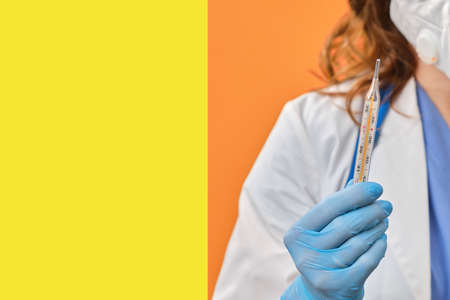 Woman doctor holds a mercury thermometer in her hand. Medical instrument for measuring body temperature, studio backgroundの写真素材