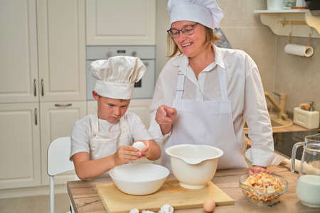 Mother and son cooking apple pie in the home kitchen. A woman and a boy in chef hats and aprons cook with pastriesの写真素材