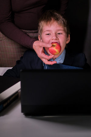 A boy in a school suit and a mother with an apple in her hand during distance learning, copy space...