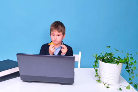 A boy in a school suit with food in his hands, copy space on a blue studio backgroundの写真素材