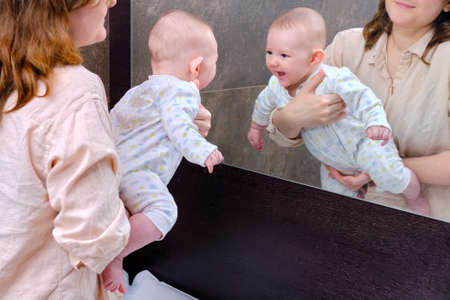 A happy baby in his mother arms saw himself in the mirror and laughsの写真素材