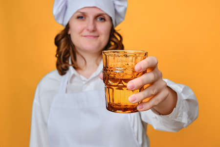 Woman chef holding a glass of water on a yellow studio backgroundの写真素材