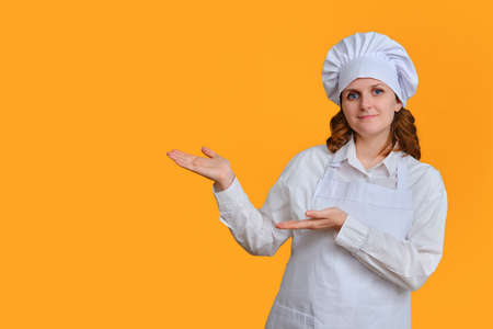 Happy woman chef on yellow studio background shows with hand on copy space for textの写真素材