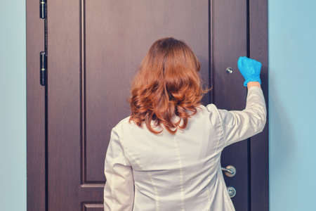 Woman doctor knocks on the door of the apartment when visiting a patient home.の写真素材