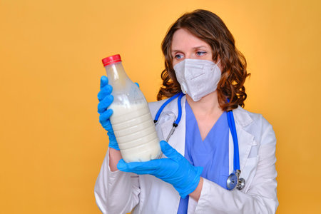 Woman doctor holding a plastic bottle with milk in her hands, yellow studio backgroundの写真素材