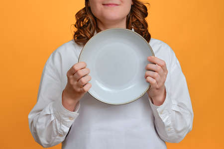 Happy woman chef with empty white plate in hand on studio background, mockup copy spaceの写真素材
