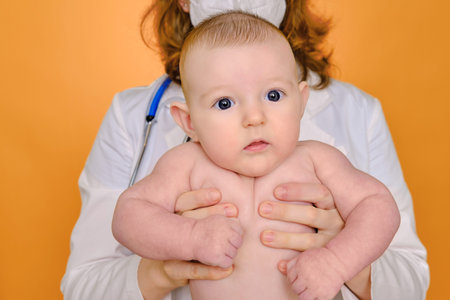 Woman pediatrician holding an infant baby in a diaper in her hands, red studio backgroundの写真素材
