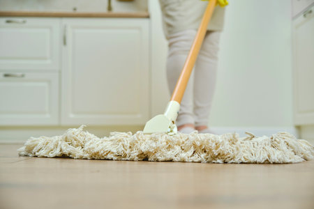A woman in an apron cleans the floor with a mop in a home kitchen