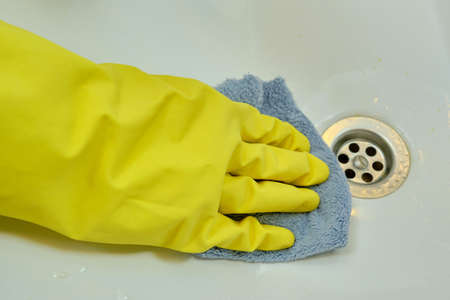 A woman is cleaning the bathroom by wiping the sink with a rag. Disinfection with yellow rubber gloves in the washroomの写真素材