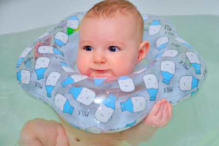Infant swimming, happy boy swims in a home bath with an inflatable ring on his neck