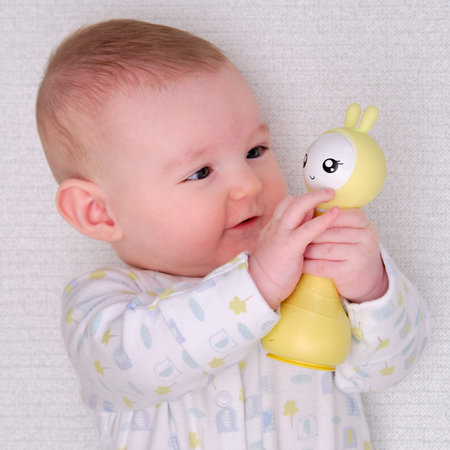 Smiling baby plays lying on the floor with toys. Four month old child on the white carpet holding a...