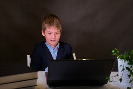 A boy in a school uniform at a computer, copy space on a dark studio background
