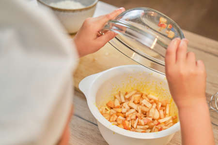 A boy in chef clothes pours apples into the dough for cooking a pieの写真素材